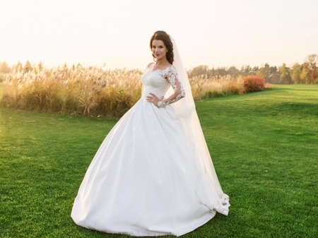 portrait of caucasian beautiful attractive woman bride in traditional european white dress standing on the field on nature backgroundの写真素材