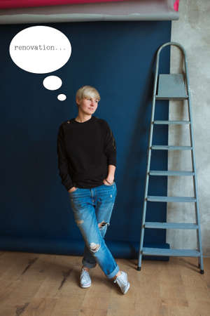Young blonde modern woman in black sweatshirt and jeans standing near ladder (stairs) and planning...