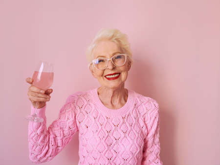 happy caucasian senior woman in cashmere pink sweater drinking rose on pink background. Celebrating, love, retirement, mature conceptの写真素材