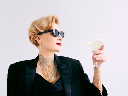 mature stylish elegant woman in tuxedo and sunglasses with glass of sparkling wine. Party, celebration, anti age conceptの写真素材