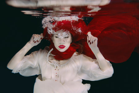 Woman in red hat and red scarf underwaterの写真素材