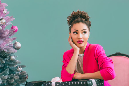 Unhappy and cheerful afro american woman with present box on the christmas tree background. Christmas, new year, happiness, holidays conceptの写真素材