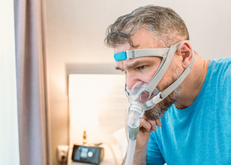 Unhappy shocked man with chronic breathing issues surprised by using CPAP machine sitting on the bed...