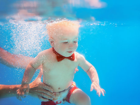 Little boy infant with red butterfly diving underwater in swimming pool, learn to swim. Sport and vacation conceptの写真素材