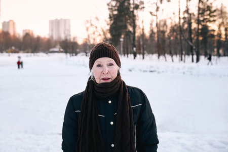 senior woman in hat and sporty jacket doing sports exercises in snow winter park. Winter, age, sport, activity, season conceptの写真素材