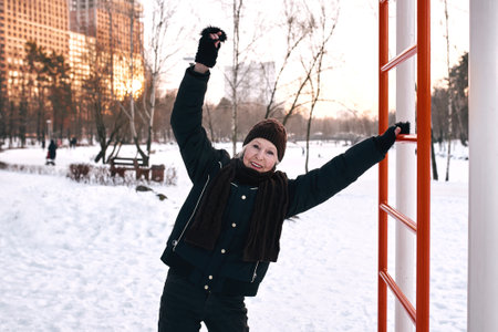 senior woman in hat and sporty jacket doing sports exercises in snow winter park. Winter, age,...