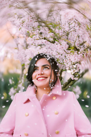Beautiful young woman in a pink coat in a blooming gardenの写真素材