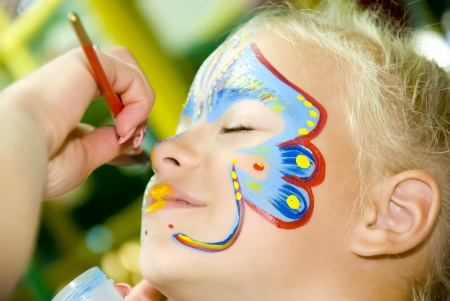 Beautiful girl with blue eyes with painted butterfly on her faceの写真素材