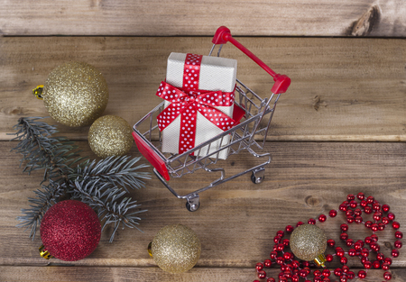Christmas shopping background composition of a multiple decoration balls and tiny shopping cart over wooden surfaceの写真素材