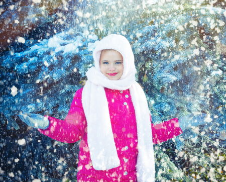Funny little girl having fun in beautiful winter park during snowfallの写真素材