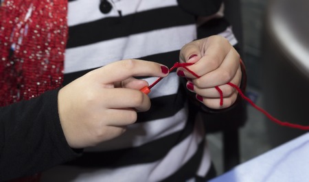 people and needlework concept - girl hands knitting with crochet hook and red yarnの写真素材