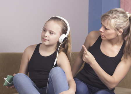 Beautiful woman is scolding her teenage daughter, girl is listening to music in headphones and ignoring her mom.の写真素材