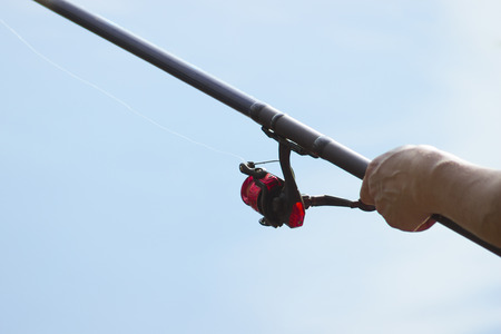 Fisherman catches a fish. Hands of a fisherman with a spinning rod in hand closeup. Spin fishing reelの写真素材