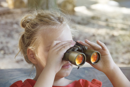 Funny little girl looking through binoculars on sunny summer day.の写真素材