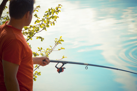 Fisherman catches a fish. Hands of a fisherman with a spinning rod in hand closeup. Spin fishing reelの写真素材
