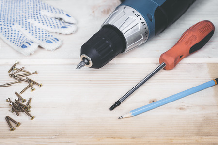 Carpenter screwing the crew with cordless screwdriver into wooden board.の写真素材