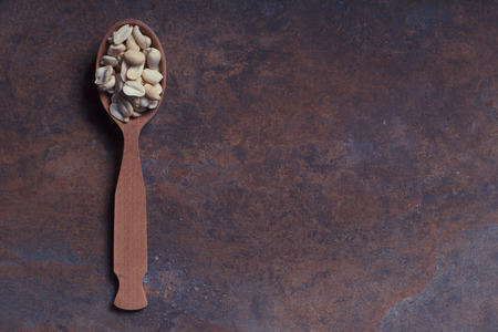Peeled roasted peanuts in a wooden spoon on a rusty backgroundの写真素材
