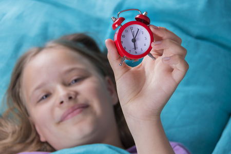 Beautiful little girl with alarm clock on bed in the bedroom