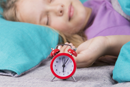 Pretty childgirl sleeping on the background of a red alarm clock that will wake her up in the...