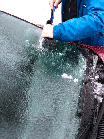 People on their morning commute in winter weather, scraping ice from their car windshieldsの写真素材