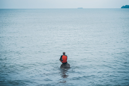 Man fishing seat on a stone patiently waiting at the seaの写真素材