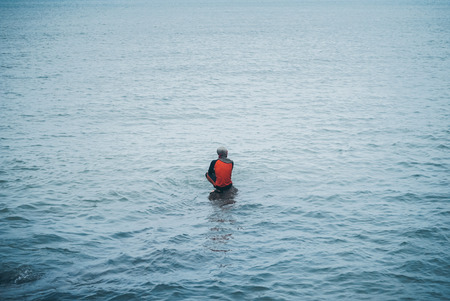 Man fishing seat on a stone patiently waiting at the sea