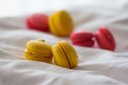 lots of colorful macaroon cakes are spread out on the white bed linen on the bed in the morningの写真素材