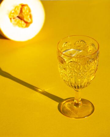 elegant yellow glass with drinking water, wine, tonic, champagne with a hard light on a yellow background with melonの写真素材