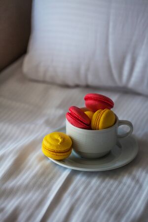 Colorful French macaron pastries in a white circle on the white linen in bed. Red and yellow pasta in natural light close-up.の写真素材