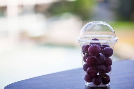 A branch of purple grapes in a transparent plastic Cup on the background of nature with a place for text. A portion of grapes from the buffet.の写真素材