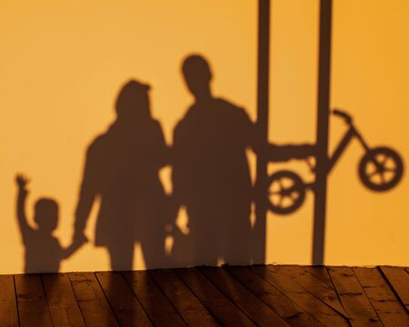 the shadow of the family with the baby and running bikes on a yellow wal