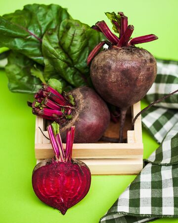 Beets whole and cut in close-up with tops on a green background with a kitchen towel.の写真素材