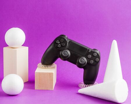 Black game joystick hanging in space, white three-dimensional geometric shapes on a purple background. Network and computer games.の写真素材