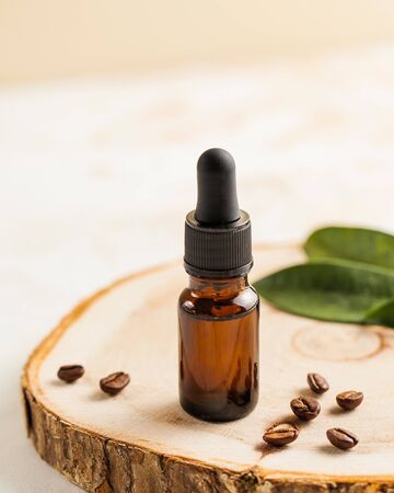Skin care. Moisturizing serum or oil for face and body close-up, next to coffee beans and green leaves on a wooden stand.の写真素材