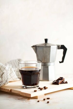 Black coffee, Moka for making espresso, geyser coffee machine on a wooden tray with coffee beans and chocolate, space for text. Photo for a coffee shop on a light background in a minimalist style.の写真素材