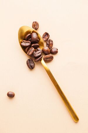 Golden teaspoon with coffee beans arabica beans on a light brown background. Vertical photo in the style of minimalism.の写真素材