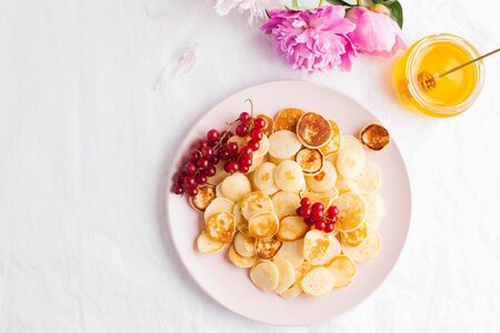Tiny pancakes with berries, honey and flowers on a white tablecloth and space for text. Pancake cereal. The concept of Breakfast, food trends. Copy space. . High quality photoの写真素材