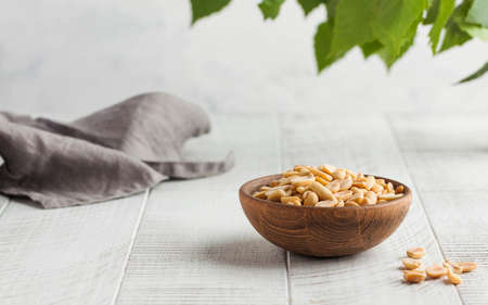 Salted peanuts in a wooden bowl on a light wooden table with green leaves in the background. Healthy snacks. Nuts.の写真素材