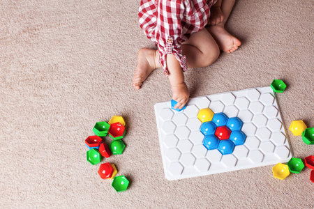 A toddler plays with a plastic mosaic on the carpet in the children's room. The concept of early development, the Montessori method.の写真素材