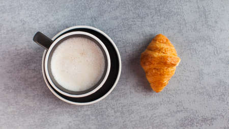 Banner coffee mug cappuccino and croissant on a gray concrete background. Minimalism. Sweet food,...