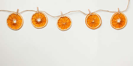 Slices of dried orange are hung on a string on top of a light background. New years background, healthy food concept.の写真素材