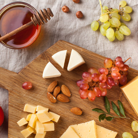 Cheese plate. Assorted cheeses on a wooden Board with grapes, honey, nuts on a linen tablecloth....