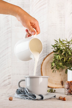 Milk is poured from a white jug into a mug. Food photos in rustic style. Concept of farm products. High quality photoの写真素材