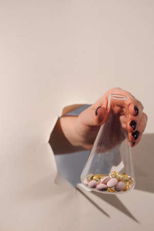 A hand holds a flask with tablets, pills breaks through a hole in the paper. Art concept of drugs,...
