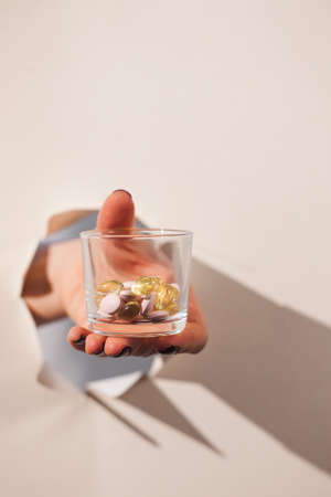 The hand holds a glass of tablets and pills breaks through a hole in the paper. Art concept of...