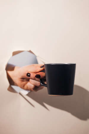 A hand holding a coffee mug through a torn paper background. Copy space.の写真素材