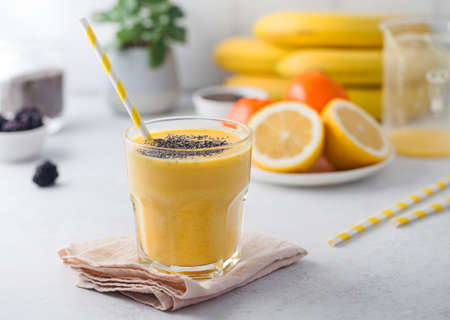 A yellow smoothie in a glass with a straw and chia seeds, fresh fruit in the background. Healthy food, detox.の写真素材