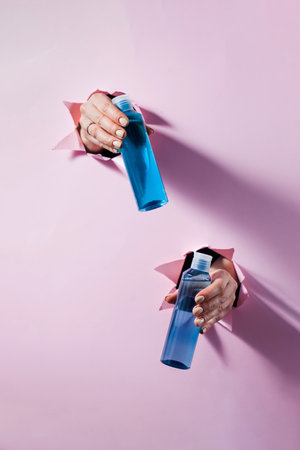 Blue cleansing lotions for skin care holds womens hands through a hole in the paper. Layout of liquid cosmetic product.の写真素材