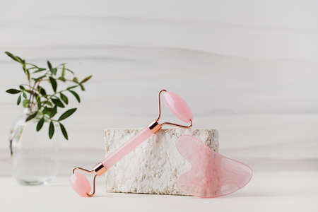 Rose quartz gua sha stone, jade roller on a light background. The concept of home skin care.