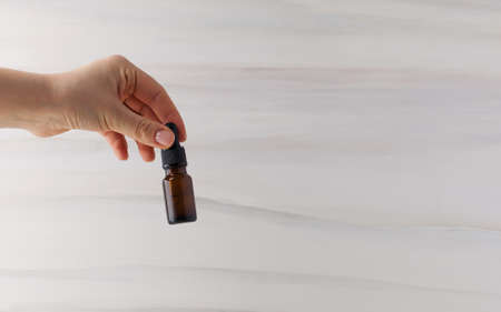 Woman holding glass dropper bottle with natural organic cosmetic against light backgroundの写真素材